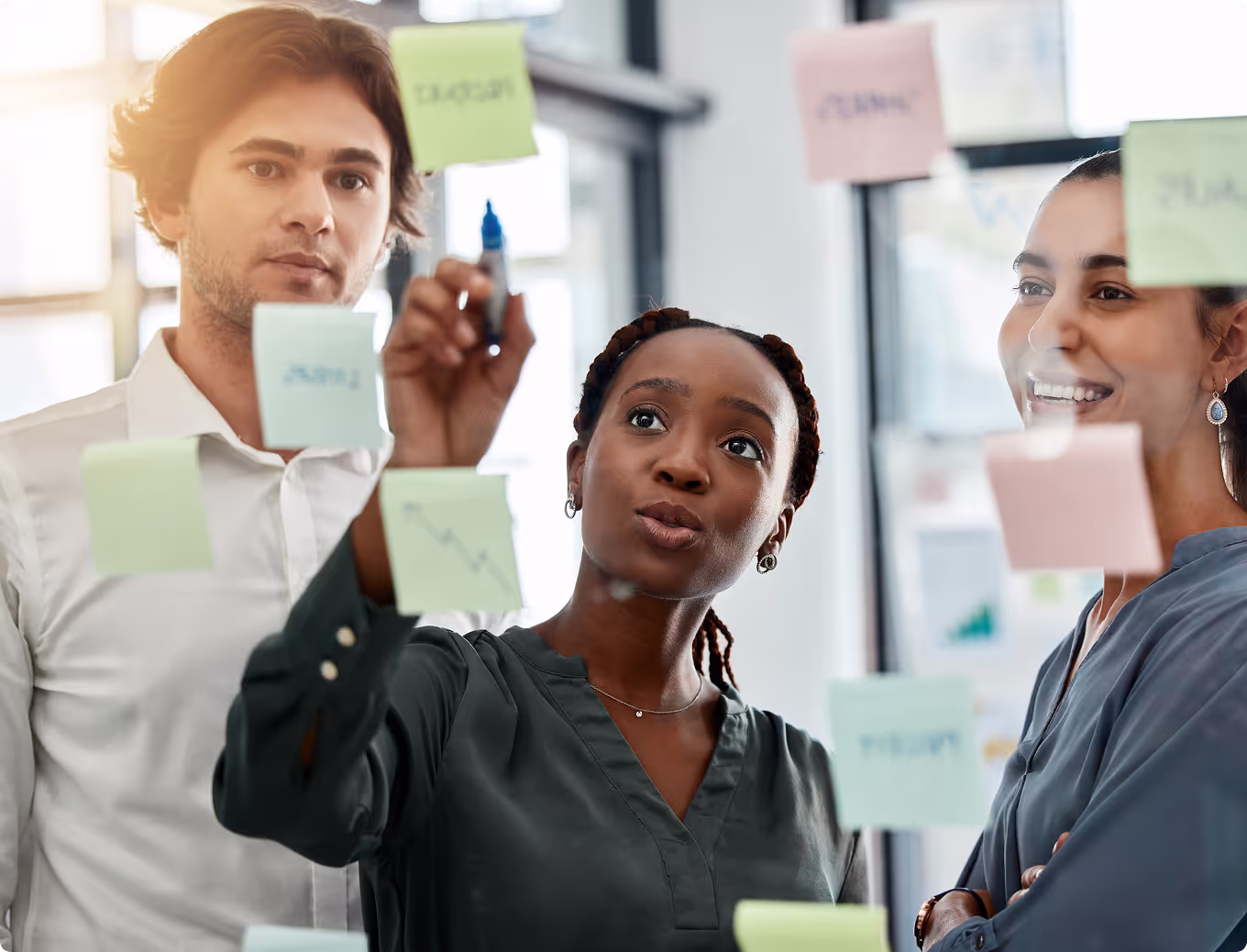 Three people are standing in front of a board with sticky notes on it.