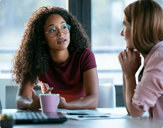 A woman in a brown jacket smiles at a man in a gray shirt.